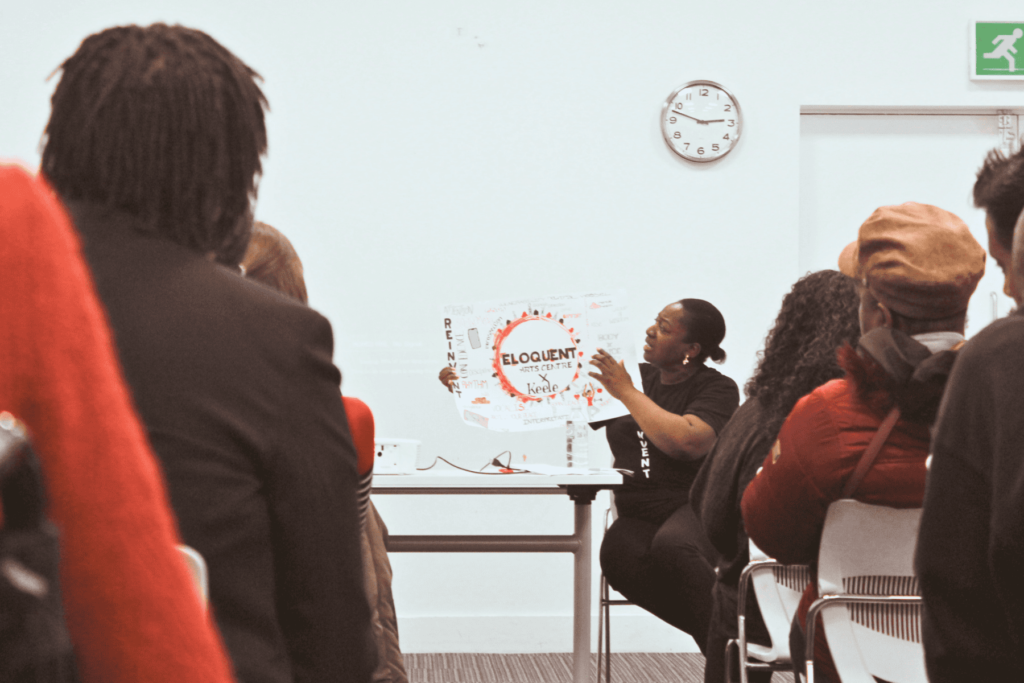 Natalie Knight presenting in a full room at community event, showing artwork produced within the REINVENT project