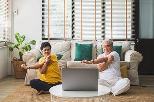 People sitting on floor and doing arm stretches whilst watching laptop screen