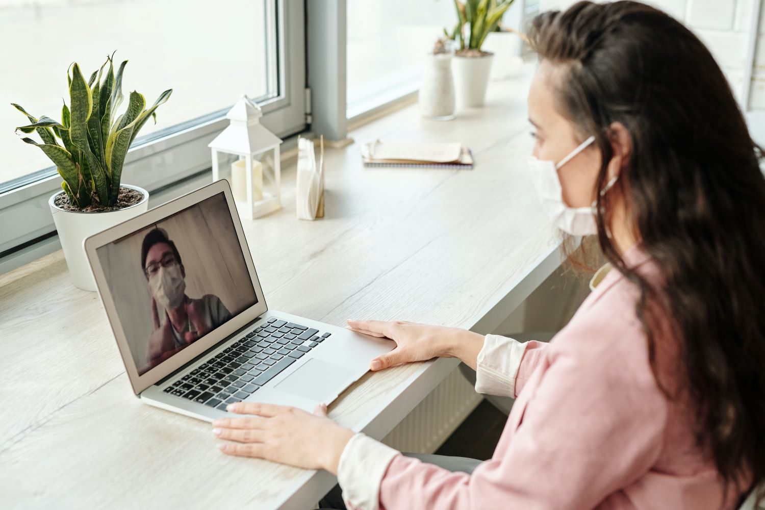 Woman using a laptop for an online consultation with a doctor, both wearing masks