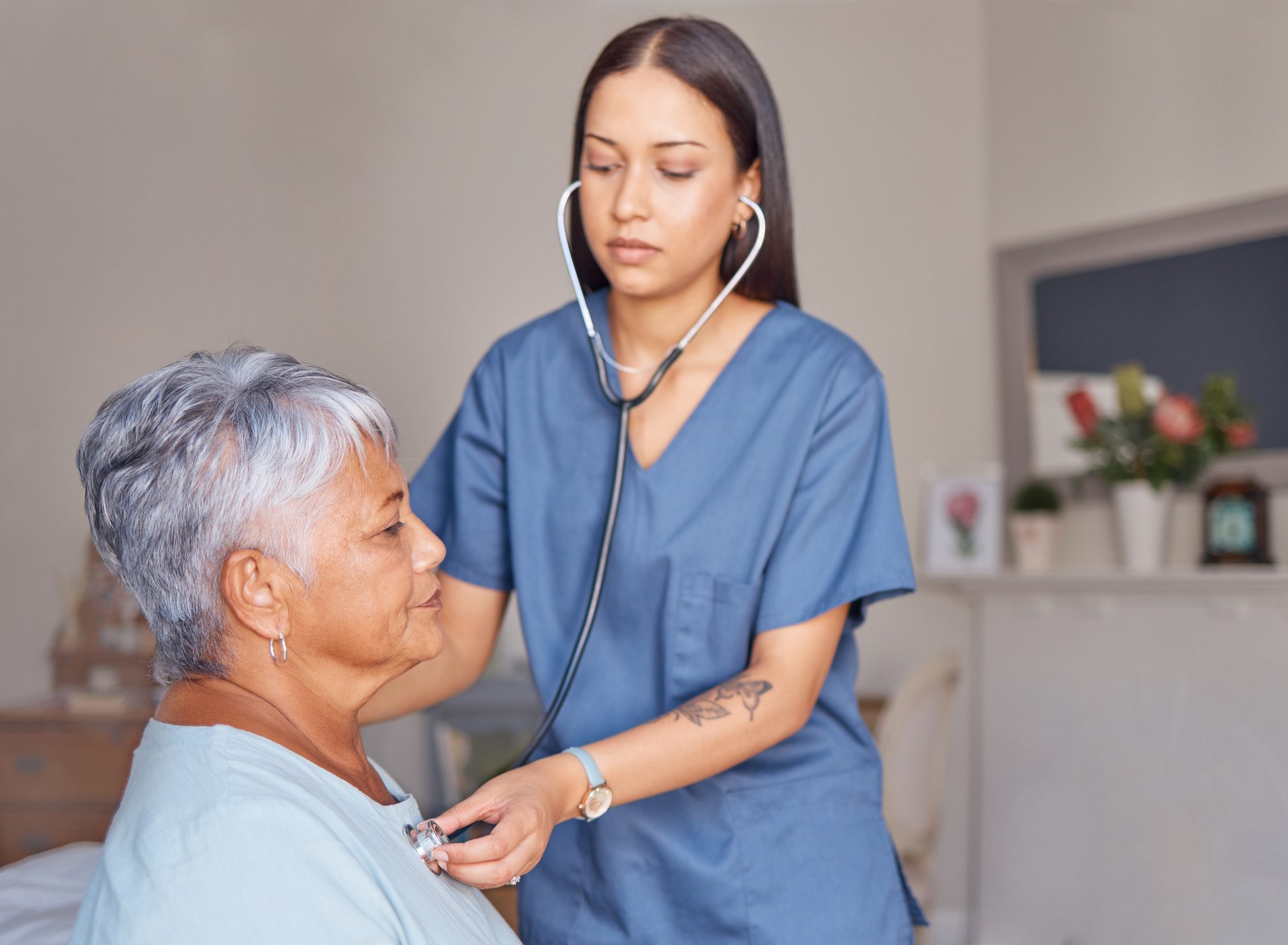 Nurse with a stethoscope listening to heartbeat of an elderly patient during a health consultation.