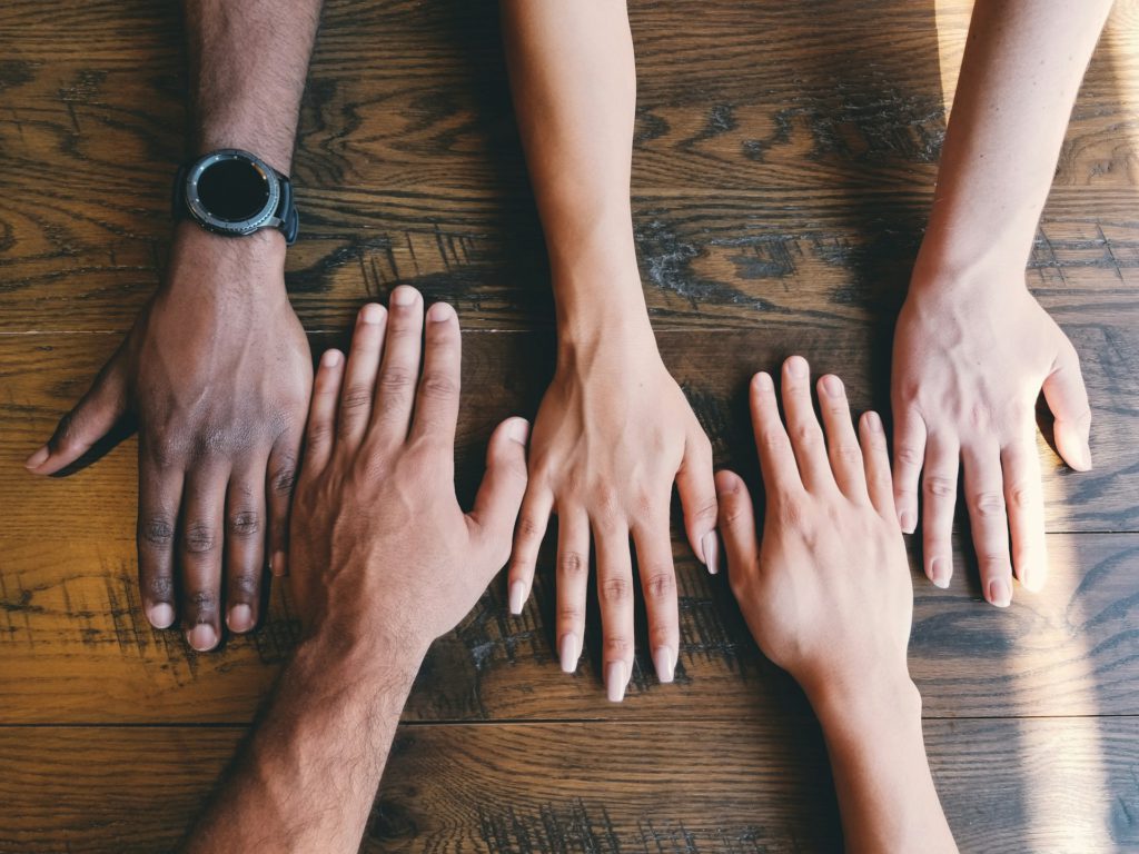 Hands of people of different ages, genders and ethnicities on a table