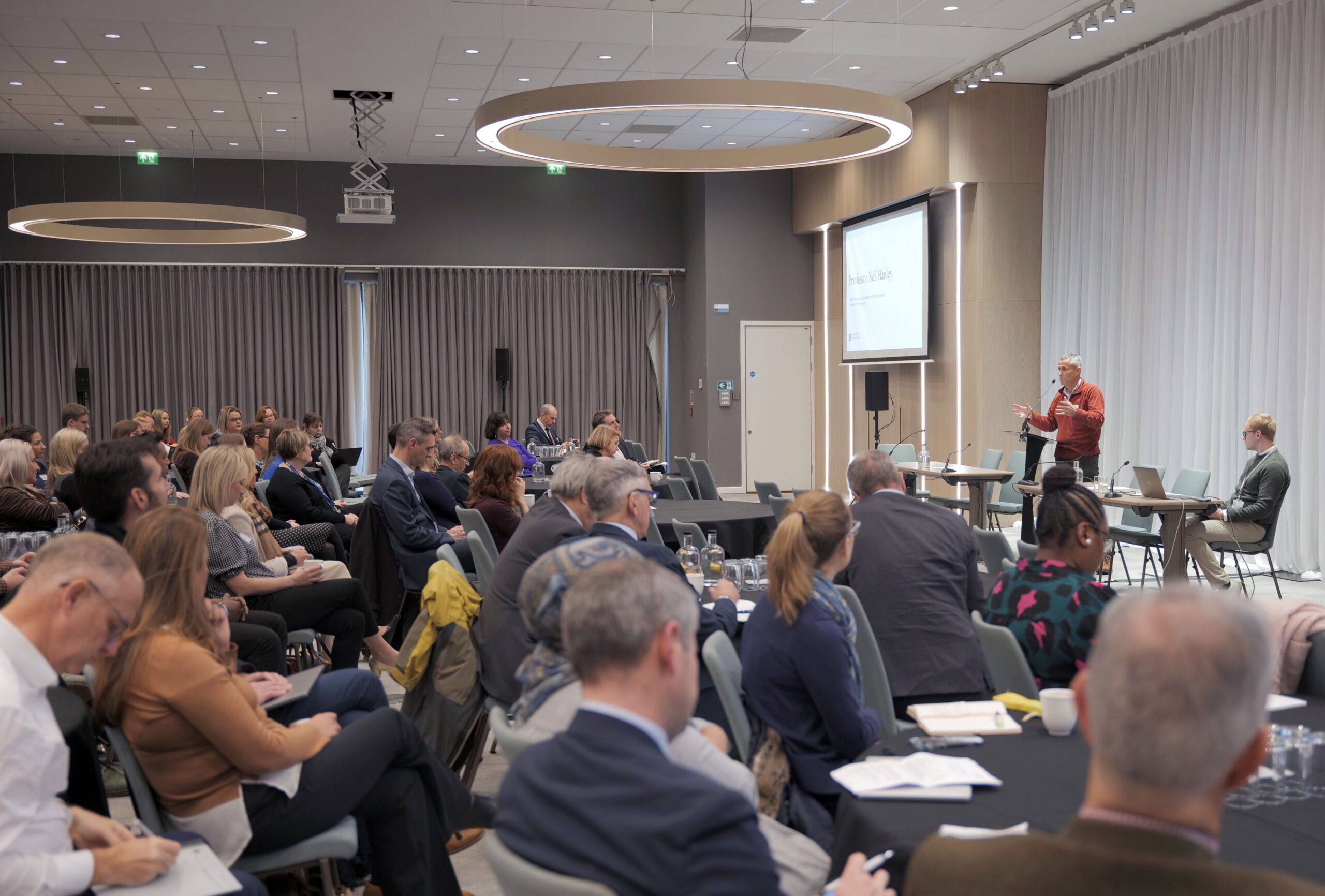 Full room of attendees at the UoB and NIHR Research Showcase, with Neil Hanley speaking on stage