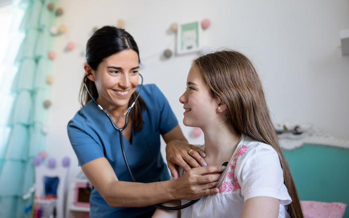 Smiling nurse checking the heart of a young patient with stethoscope