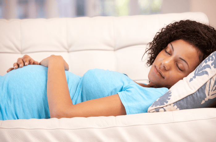 Pregnant woman laying down on sofa and resting