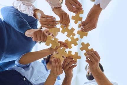 People's hands holding individual jigsaw pieces.