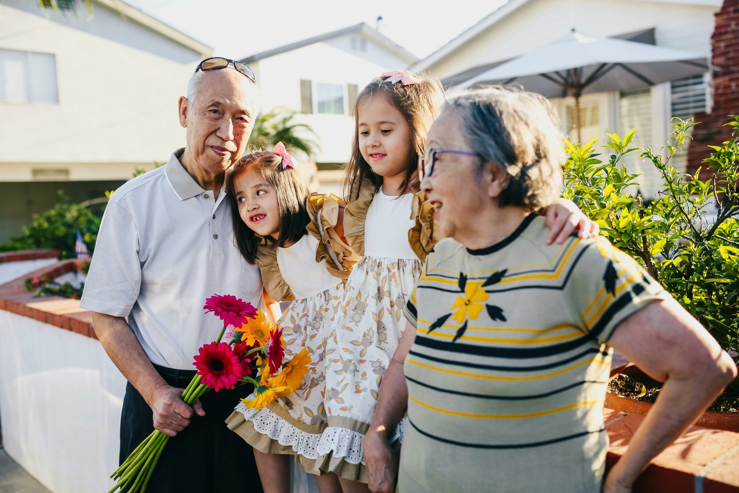 Asian grandparents with two grand-daughters, sitting outside a building in the sun