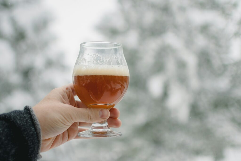 Person holding beer glass with background of a snowy forest