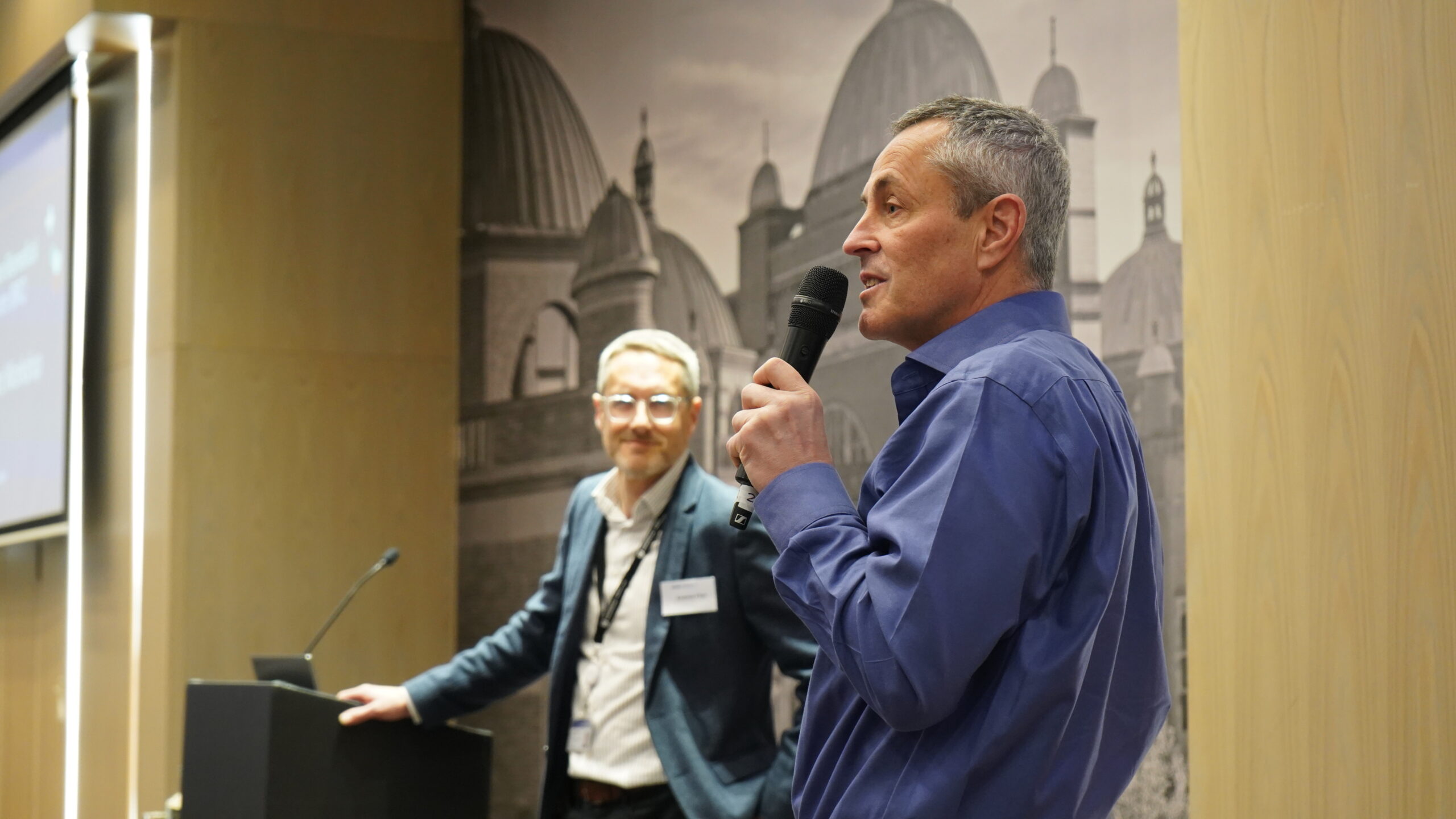 Prof Neil Hankey talking on stage with Prof Andrew Filer in the background