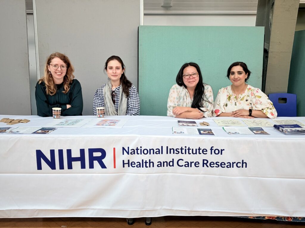 Four women sitting at a table covered by an NIHR branded tablecloth
