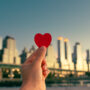 Hand holding paper heart with the backdrop of a city landscape
