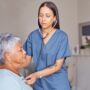 Nurse with a stethoscope listening to heartbeat of an elderly patient during a health consultation.
