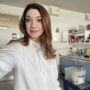 A selfie of a brown haired woman wearing a lab coat and standing in a science lab