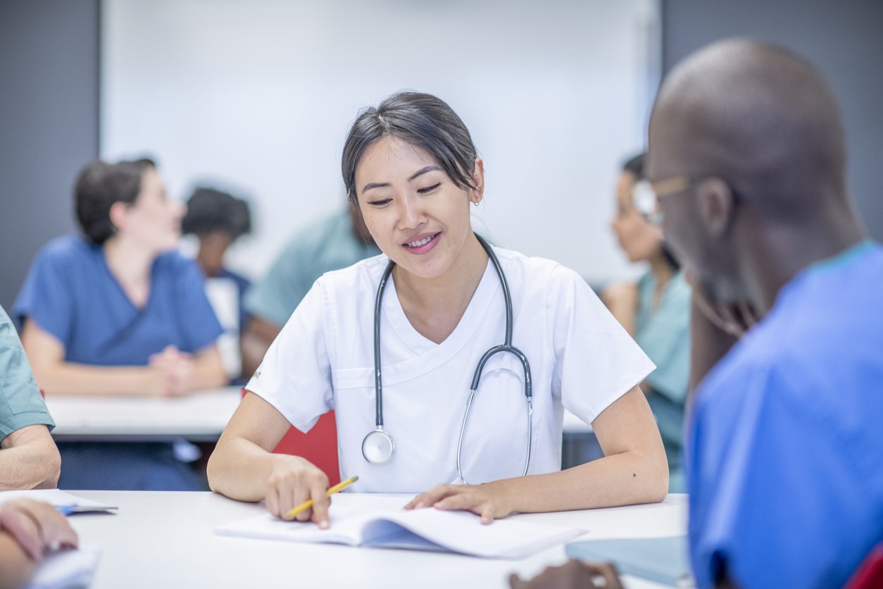 Healthcare professional with stethoscope around neck writes on notebook during training session with colleagues