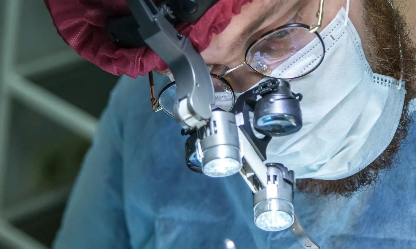 Surgeon wearing face mask examining patient with headmounted binoculars and headlight