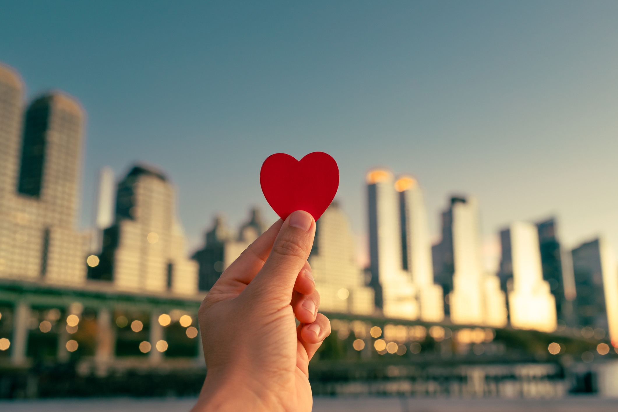 Hand holding paper heart with the backdrop of a city landscape
