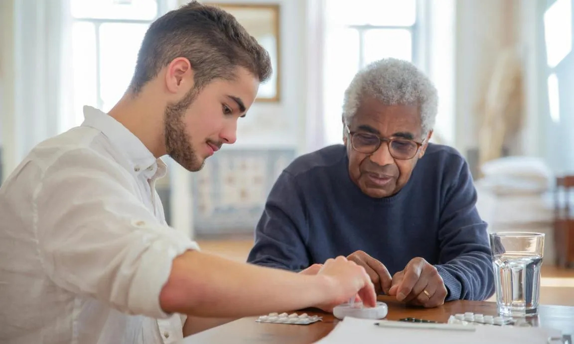 Young man assisting an older man in taking medicines