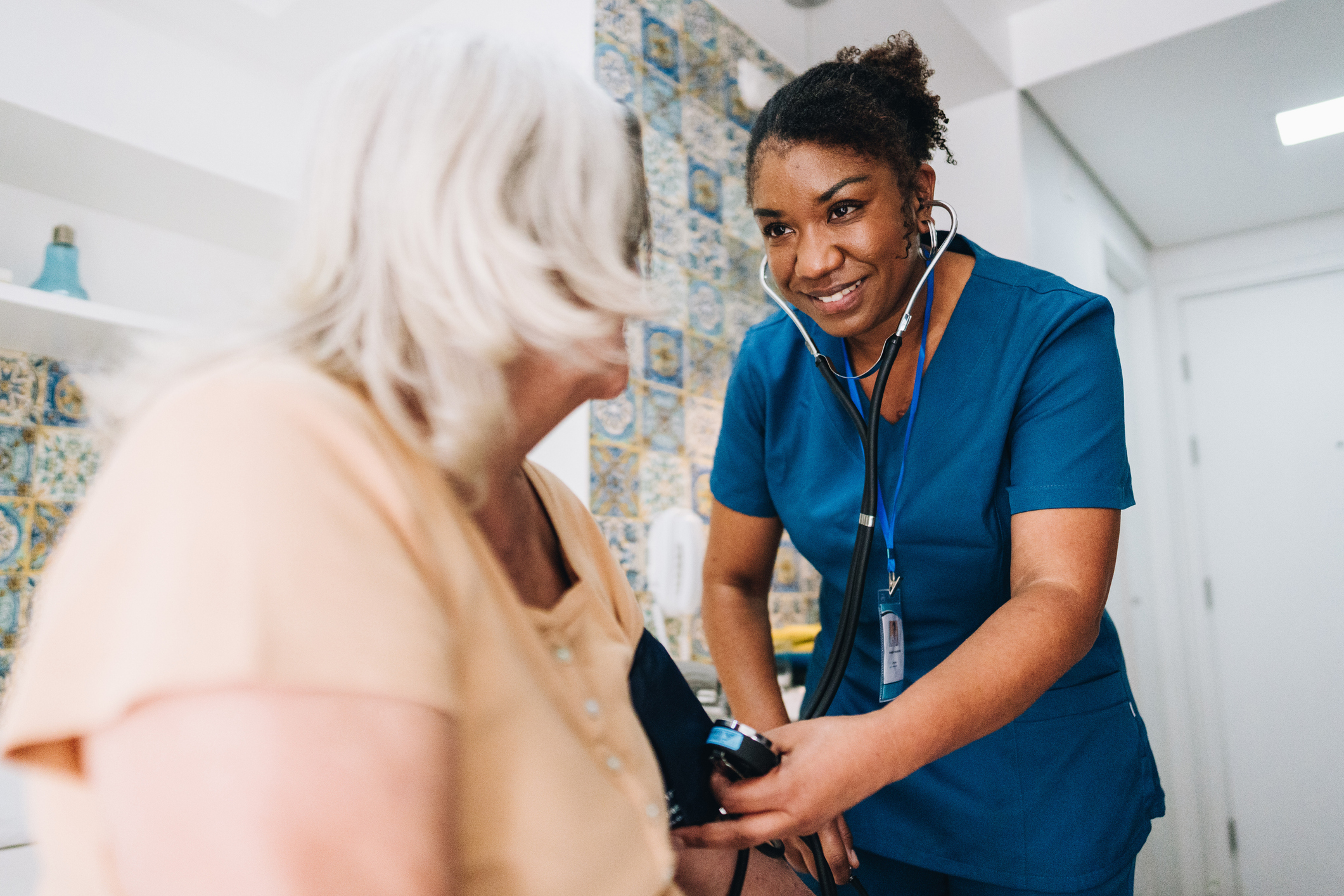 nurse taking blood pressure and listening to heart of senior woman at home